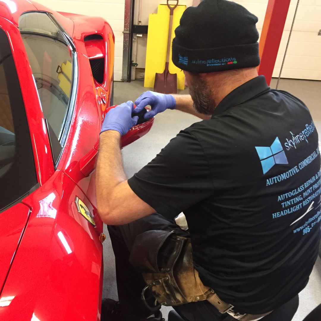 Gloved Skyline Reflections installer working protective film onto the front fender and door edge of a red sports car in the Hamilton shop