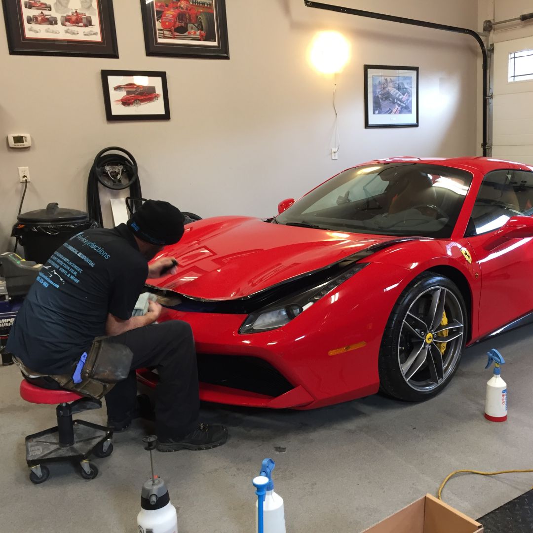 Skyline Reflections installer working along the front end of a red sports car in the Hamilton shop
