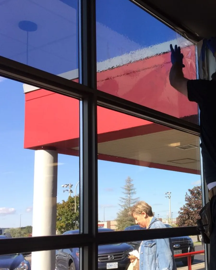 Installer working film across the upper pane of a tall storefront window
