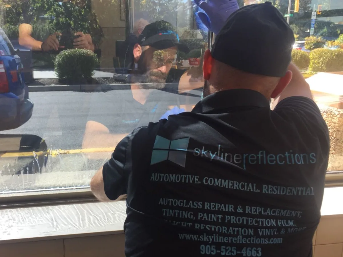 Skyline Reflections installer applying architectural window film to a large commercial storefront window in Hamilton
