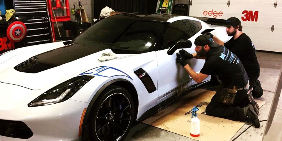 Installer working film onto the front end of a white performance car