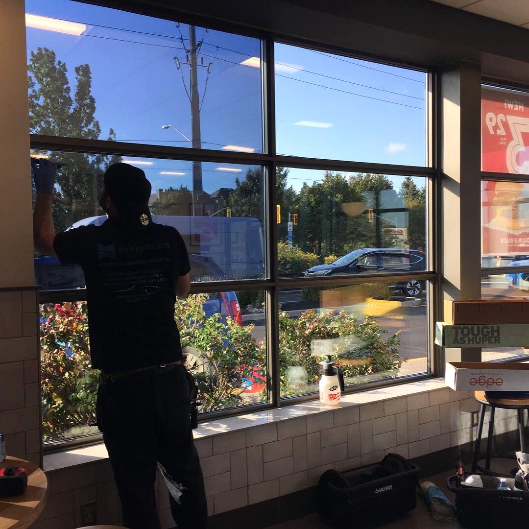 Skyline Reflections installer applying architectural window film to a commercial window bank from inside the building