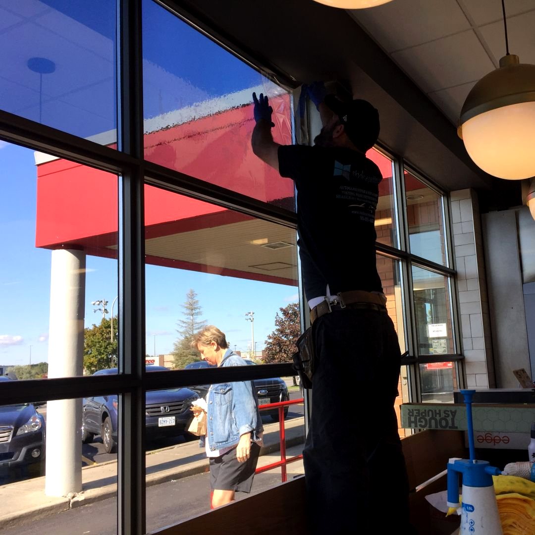 Skyline Reflections installer working across a measured commercial window bank before film installation