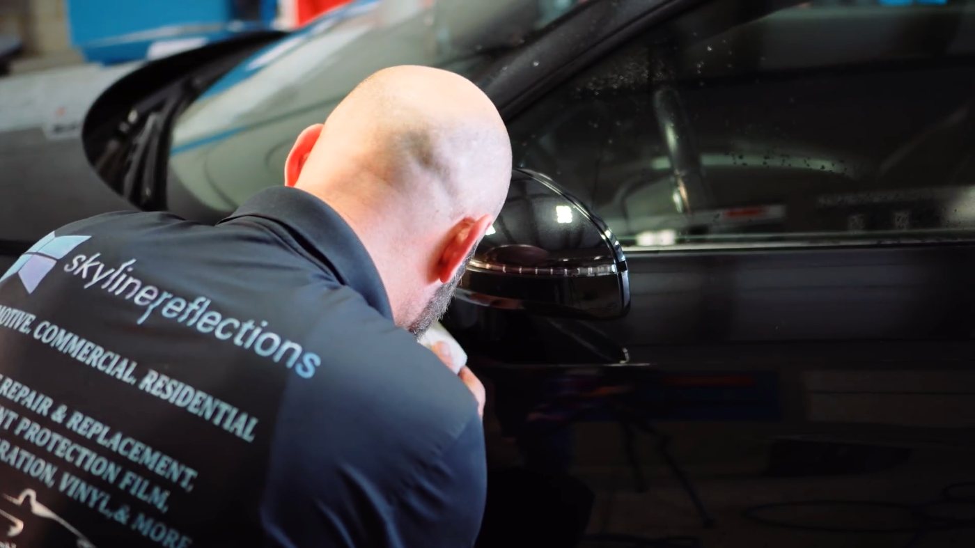 Skyline Reflections installer working along the glass and mirror line of a black vehicle