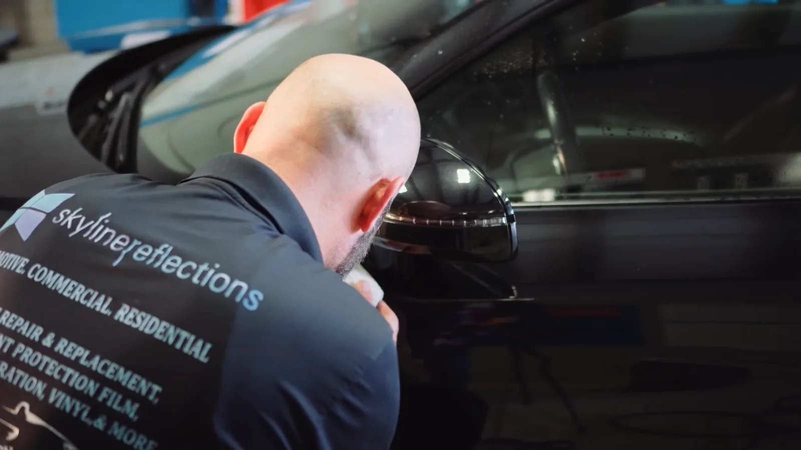 Skyline Reflections installer working along the door glass and mirror line of a glossy black vehicle inside the Hamilton shop
