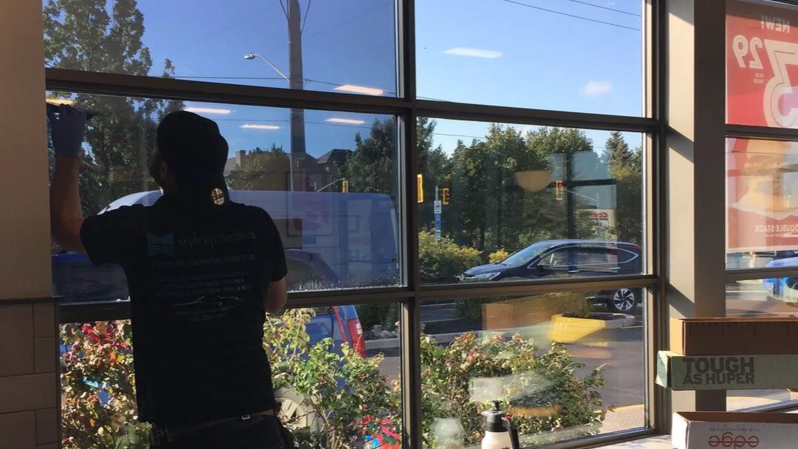 Installer applying film to a storefront window from inside, with daylight coming through the glass