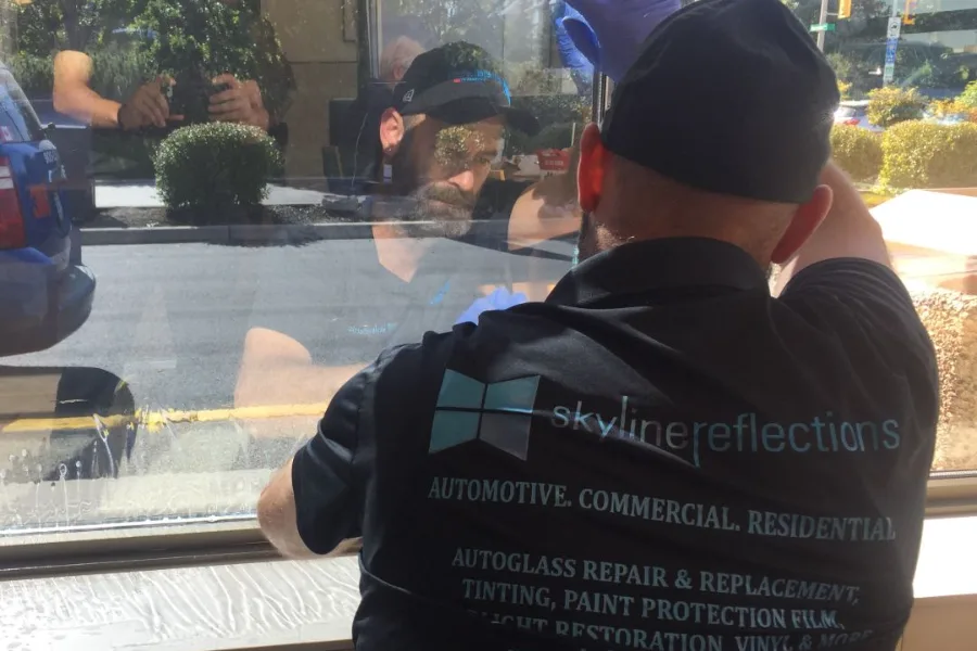 Skyline Reflections installer working film against a large ground-floor window from inside