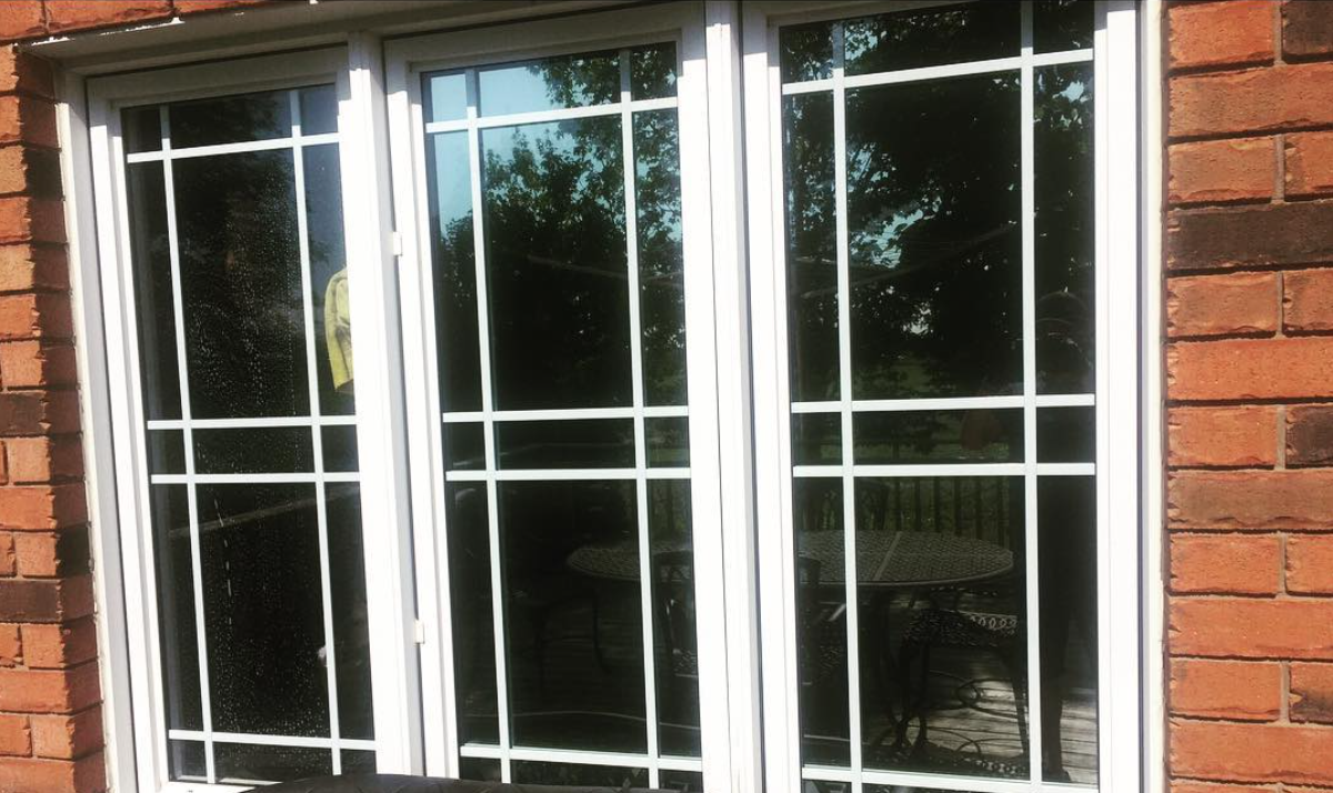 Finished residential garden doors in a brick wall, the treated glass reflecting trees and a patio table