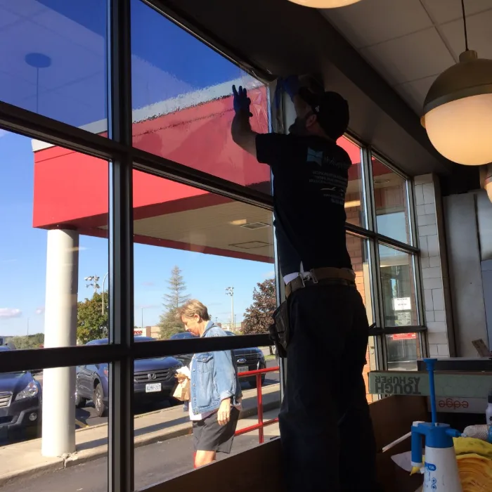 Skyline installer squeegeeing film onto a commercial window from inside the unit