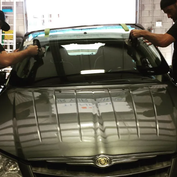 Two installers setting a replacement windshield into a vehicle